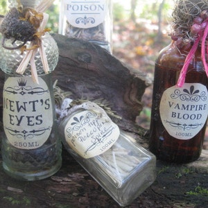 May include: Three glass bottles with labels and different colored liquids. The labels read "Newt's Eyes", "Poison Hipped Porcupine Spine", and "Vampire Blood". The bottles are sitting on a wooden surface.