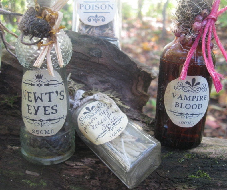 May include: Three glass bottles with labels and different colored liquids. The labels read "Newt's Eyes", "Poison Hipped Porcupine Spine", and "Vampire Blood". The bottles are sitting on a wooden surface.