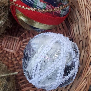 May include: Two handmade Christmas ornaments in a wicker basket. One ornament is red with gold trim and plaid fabric. The other ornament is white with silver and black lace.
