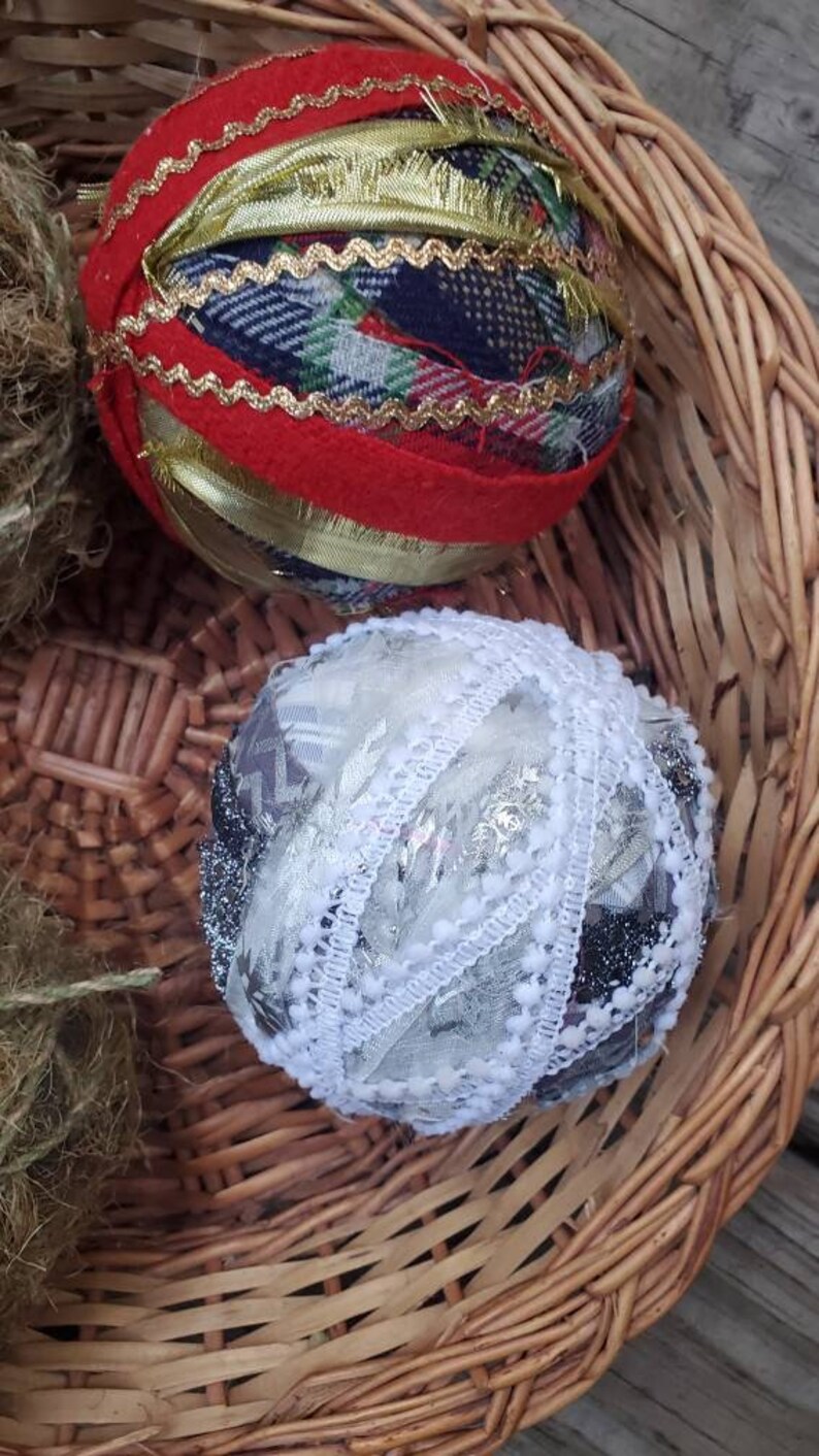 May include: Two handmade Christmas ornaments in a wicker basket. One ornament is red with gold trim and plaid fabric. The other ornament is white with silver and black lace.