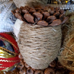 May include: A brown pine cone wrapped in twine, surrounded by other natural elements in a wicker basket.