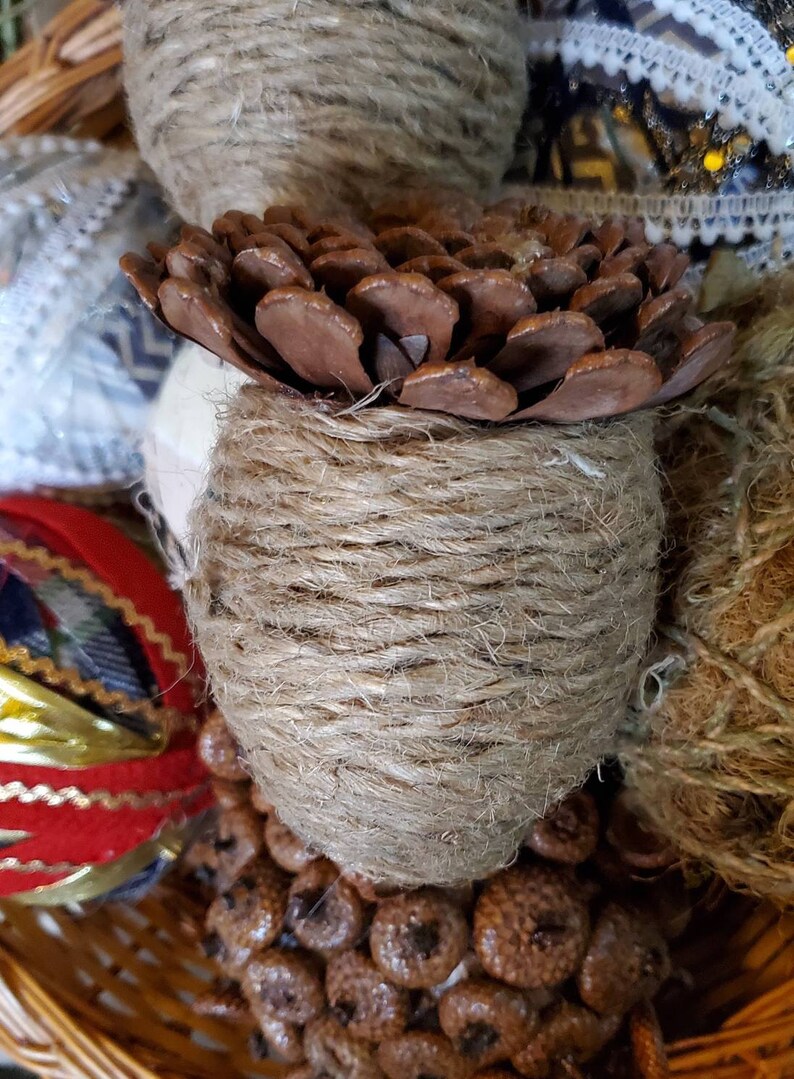May include: A brown pine cone wrapped in twine, surrounded by other natural elements in a wicker basket.