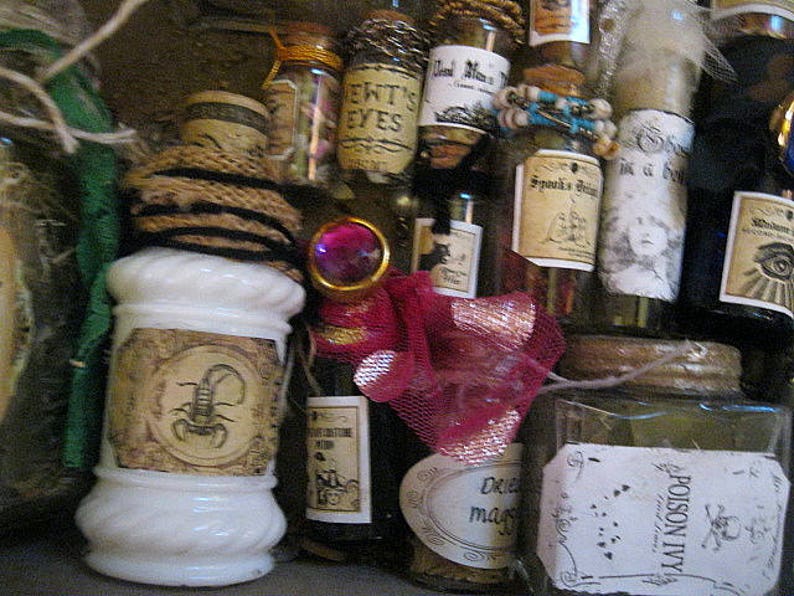 May include: A collection of small glass bottles with various labels and contents. Some bottles are tied with twine and have cork stoppers. The labels include text such as "EWT'S EYES", "Spook's Brew", and "Poison Ivy".
