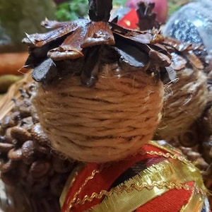 May include: A close-up of a Christmas ornament made from a pine cone wrapped in twine. The ornament is decorated with a red and gold ribbon. The ornament is sitting in a wicker basket.