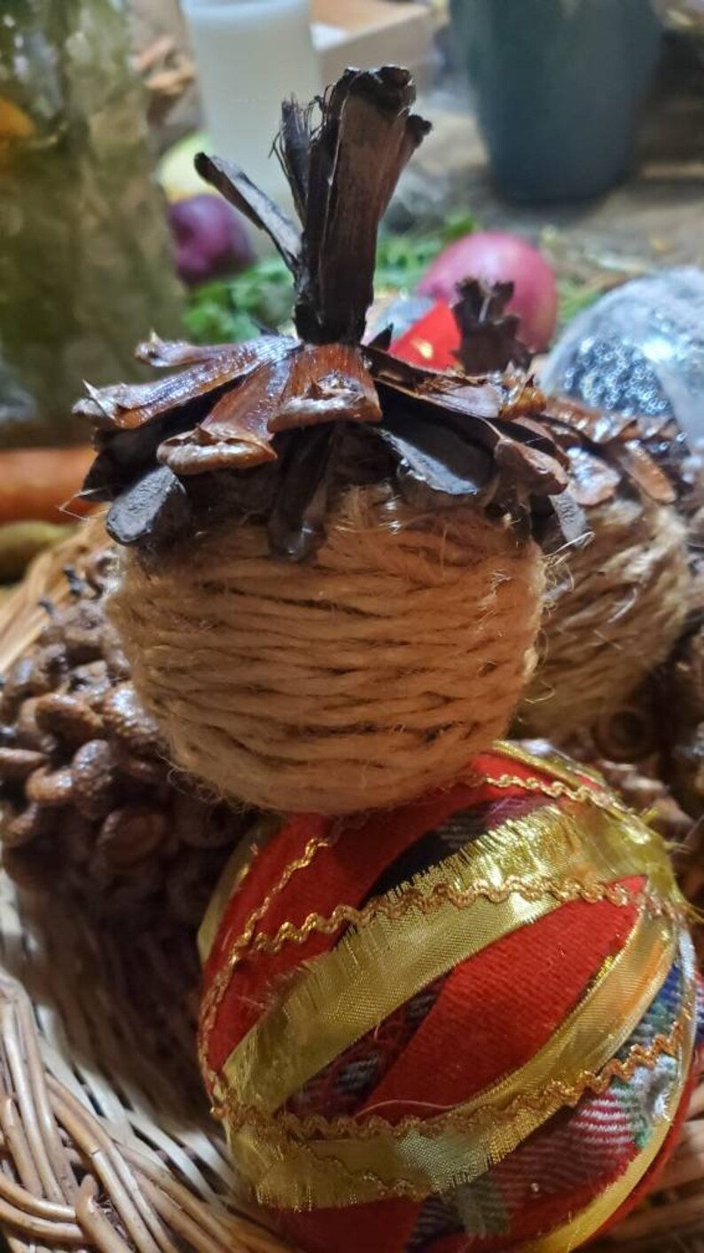 May include: A close-up of a Christmas ornament made from a pine cone wrapped in twine. The ornament is decorated with a red and gold ribbon. The ornament is sitting in a wicker basket.