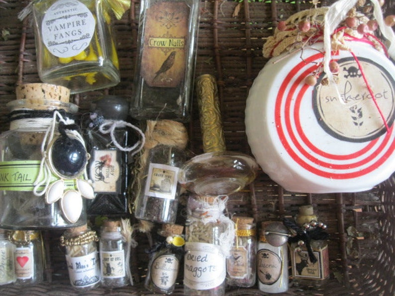 May include: A collection of small glass bottles with various labels and contents, including "Vampire Fangs", "Crow Nails", "Ink Tail", "Dried Maggot", and "Snake Root". The bottles are arranged in a wicker basket with a white and red striped lid.