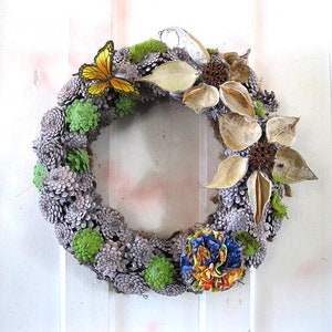 May include: A wreath made of pine cones, moss, and dried flowers. The wreath is decorated with a yellow butterfly and a colorful fabric flower.
