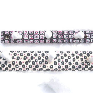 Könnte beinhalten: Zwei Holz-Kleiderständer mit einem geometrischen Muster in Schwarz und Weiß und rosa Akzenten. Jeder Kleiderständer hat fünf weiße Pompon-Knöpfe.