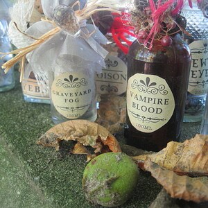 May include: A collection of small glass bottles with labels that read "Graveyard Fog", "Vampire Blood", "Ewt Eye", and "Poison Porco Spirit". The bottles are filled with a variety of liquids and are decorated with various embellishments, including a small, white, lace-like bow.