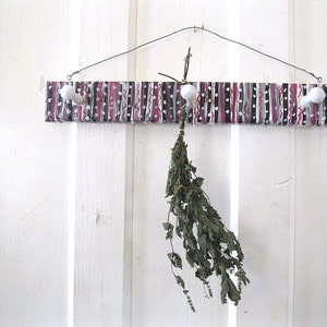 May include: A wooden coat rack with three white hooks and a black and white striped design. A bunch of dried herbs hangs from one of the hooks.