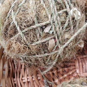 May include: A close-up of a brown wicker basket filled with two round balls of natural twine and dried grasses. The balls are wrapped with twine and have a rustic, natural look.