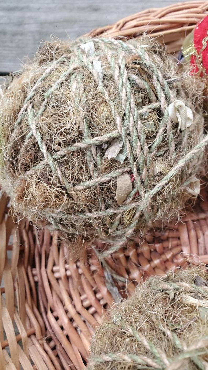 May include: A close-up of a brown wicker basket filled with two round balls of natural twine and dried grasses. The balls are wrapped with twine and have a rustic, natural look.