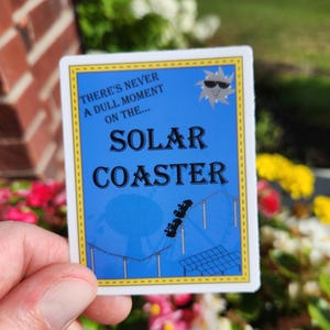 May include: A rectangular sticker with a blue background and yellow border. The sticker features the words "THERE'S NEVER A DULL MOMENT ON THE... SOLAR COASTER" and a cartoon sun wearing sunglasses. A roller coaster graphic is also included.