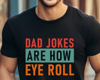 May include: A black t-shirt with the text "DAD JOKES ARE HOW EYE ROLL" in red, orange, and teal. The text is in a retro style font.