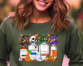 May include: Green crewneck sweatshirt featuring a Halloween-themed graphic. The graphic includes illustrations of medicine bottles, a skull, witch hats, pumpkins, a ghost, and the text "Midazolam", "Diprivan", "Fentanyl", and "Ativan".