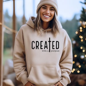 May include: A beige hoodie with a black graphic that says "CREATED with a purpose" and a cross.