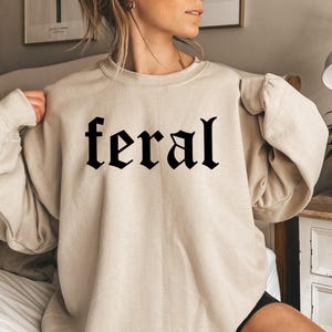 May include: A beige sweatshirt with the word "feral" printed in black gothic lettering.