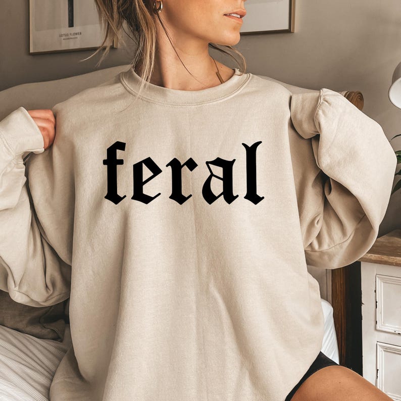 May include: A beige sweatshirt with the word "feral" printed in black gothic lettering.