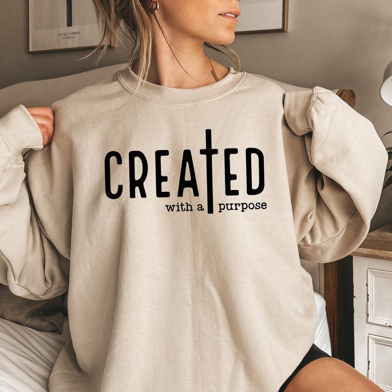May include: A beige sweatshirt with the text "CREATED with a purpose" and a cross graphic printed on the front.