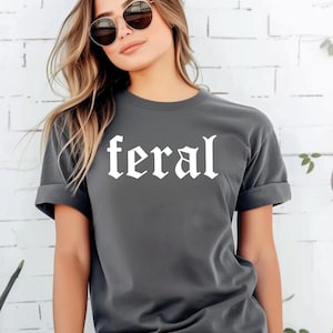 May include: A dark grey t-shirt with the word "feral" printed in white in a gothic font.