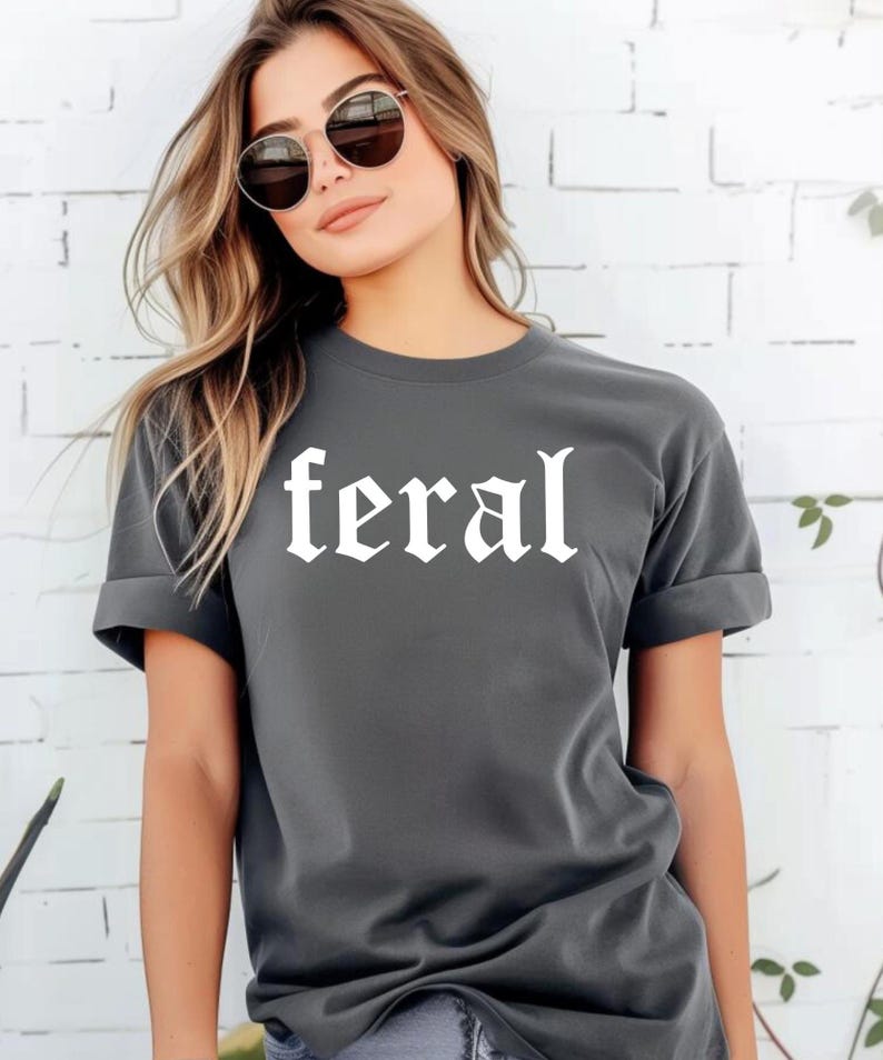 May include: A dark grey t-shirt with the word "feral" printed in white in a gothic font.