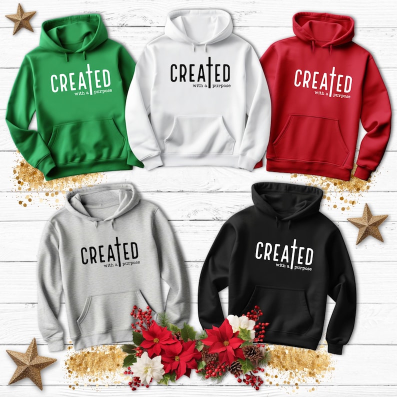 May include: Five hooded sweatshirts in different colors, each with the text "CREATED with a purpose" and a cross symbol printed on the front. The sweatshirts are displayed on a wooden background with Christmas decorations.