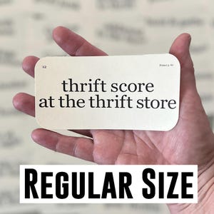 May include: A rectangular card with the text "thrift score at the thrift store" in black font. The card also has the text "Primer p. 60" and "12". Below the card is the text "REGULAR SIZE" in a bold, black font.