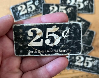 Può includere: Un'etichetta di prezzo vintage in bianco e nero con il testo "25¢ North Pole General Store" in lettere bianche.