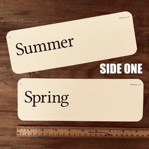 May include: Two cream-colored index cards with black text. The top card says "Summer" and the bottom card says "Spring". The cards are labeled "Primer p. 21" and "Primer p. 20" respectively. The text "SIDE ONE" is printed in black on a white background.