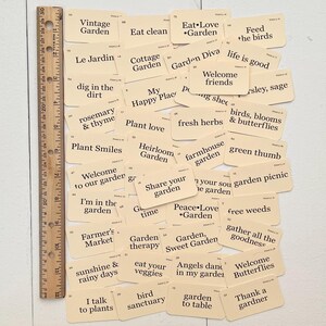 Pu&ograve; includere: Una collezione di carte beige con testo nero, ciascuna con una frase diversa sul tema del giardinaggio. Alcune delle frasi includono "Mangia pulito", "Diva del giardino", "Amore per le piante", "Benvenuti amici", "Pollice verde", "Terapia del giardino", "Gli angeli danzano nel mio giardino" e "Grazie a un giardiniere".
