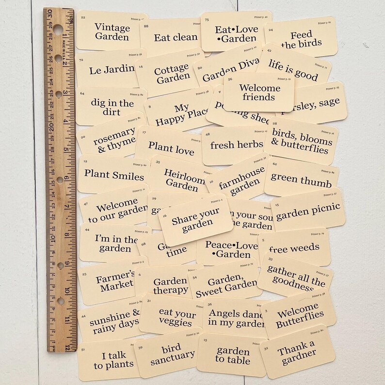 Pu&ograve; includere: Una collezione di carte beige con testo nero, ciascuna con una frase diversa sul tema del giardinaggio. Alcune delle frasi includono "Mangia pulito", "Diva del giardino", "Amore per le piante", "Benvenuti amici", "Pollice verde", "Terapia del giardino", "Gli angeli danzano nel mio giardino" e "Grazie a un giardiniere".