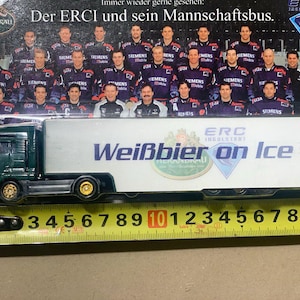 Puede incluir: Un camión de juguete verde con un remolque blanco. El remolque tiene el texto "ERC Ingolstadt Weißbier on Ice" impreso. El camión mide 25,4 cm de largo.