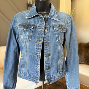 May include: A light blue denim jacket with a classic design. The jacket features a collared neckline, button-down front, and two chest pockets. The jacket is displayed on a black mannequin.