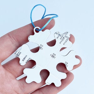 Könnte beinhalten: Ein weißer, schneeflockenförmiger Anhänger mit einer blauen Schnur. Der Anhänger hat Text darauf, darunter "R69", "D20", "R70", "R71", "D33", "D34", "D35", "R53", "R54", "R55" und "R56".
