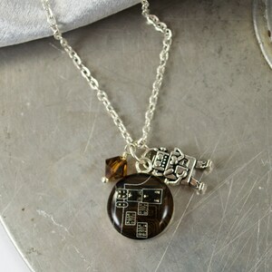 Könnte beinhalten: Eine silberne Kettenkette mit einem braunen Leiterplattenanhänger, einem kleinen silbernen Roboteranhänger und einem braunen Kristallanhänger.