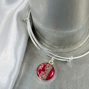 May include: A silver bangle bracelet with a red circuit board charm. The charm is round and has a clear epoxy coating.