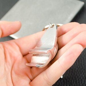 May include: A silver bottle opener keychain with a key ring. The opener is shaped like a bottle opener with a small handle.