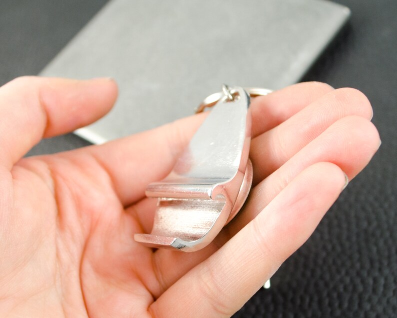 May include: A silver bottle opener keychain with a key ring. The opener is shaped like a bottle opener with a small handle.