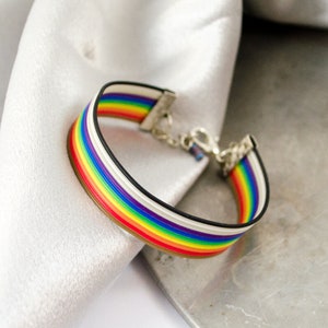 May include: A rainbow-colored silicone bracelet with a silver clasp. The bracelet is made of multiple bands of color, including red, orange, yellow, green, blue, indigo, and violet.