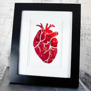Puede incluir: Una impresión enmarcada de un corazón anatómico rojo hecho con piezas de placa de circuito.