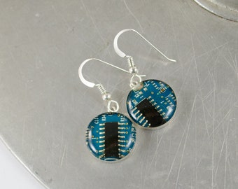 May include: A pair of silver earrings with round blue resin pendants featuring a circuit board design.