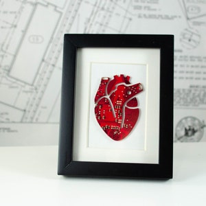May include: A black framed picture featuring a red circuit board heart. The heart is crafted from electronic components, creating a unique and contemporary piece of art.