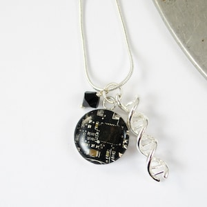 Könnte beinhalten: Eine silberne Halskette mit einem schwarzen Leiterplattenanhänger, einem schwarzen Kristallanhänger und einem silbernen DNA-Helix-Anhänger.