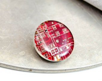May include: A round, red, clear resin cabochon with a circuit board design. The design features the text "C374", "C372", "C385", and "C390".