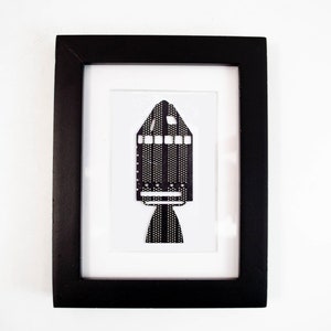 May include: A black and white framed print of a rocket ship made from paper.