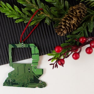 May include: A green circuit board Christmas ornament shaped like a computer monitor with a red string for hanging.
