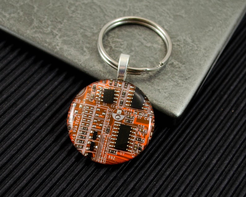 May include: A round, orange and black keychain with a circuit board design. The keychain is attached to a silver key ring.