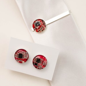 May include: Three cufflinks with red circuit board designs. The cufflinks are on a white surface. The cufflinks are a great way to add a touch of personality to your outfit.