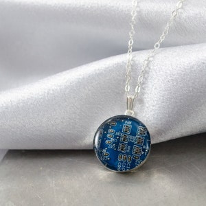 May include: A silver chain necklace with a round pendant featuring a blue circuit board design.