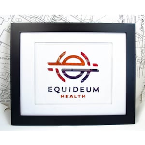 May include: Framed artwork featuring the "EQUIDEUM HEALTH" logo. The logo is a stylized design in orange, red, and purple, set against a white background. The artwork is encased in a black frame with a white mat.